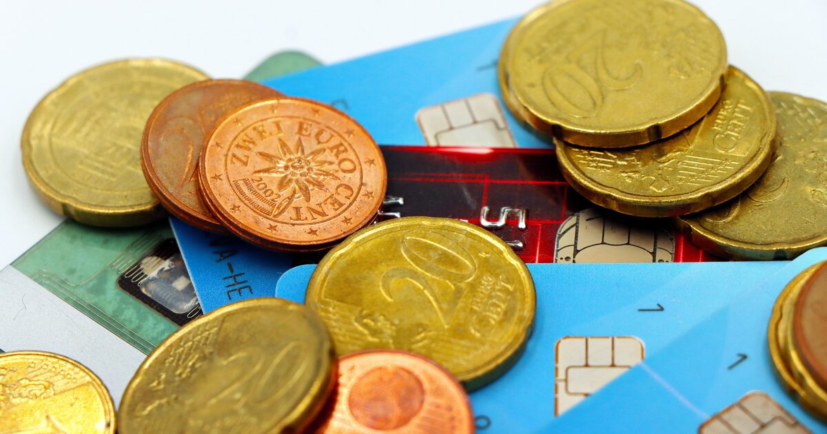 Gold and copper coins piled on top of payment cards on a desk