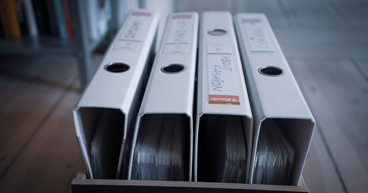 A row of ring binders with plastic sleeves stored upright in a wooden box