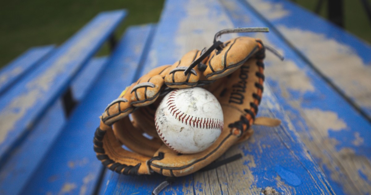 A vintage baseball and leather glove resting on a weathered blue wooden bench
