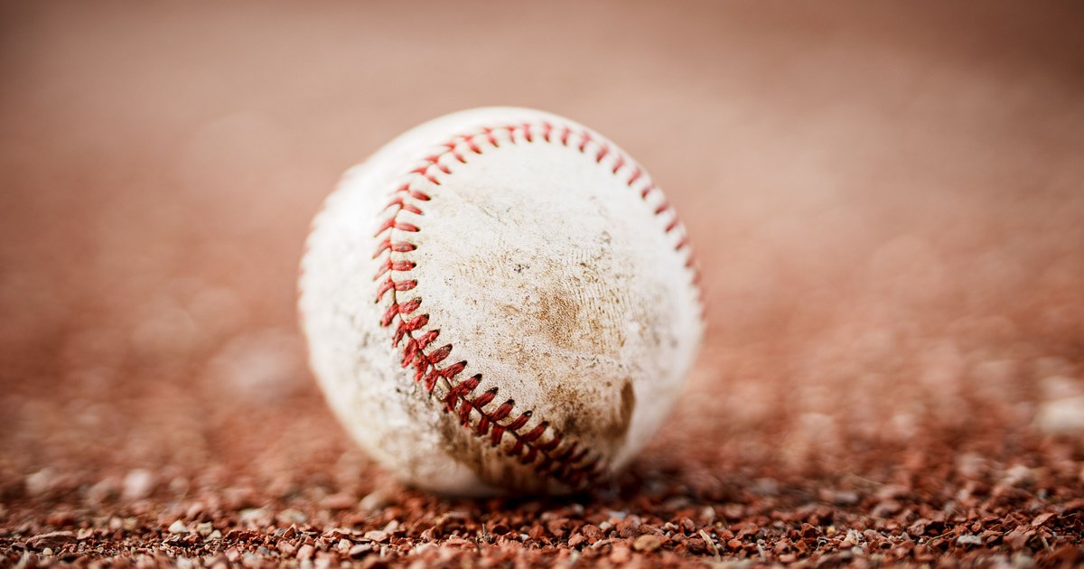 A worn baseball resting on gravel infield dirt, close up