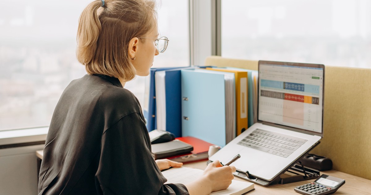 A person checking a spreadsheet on a laptop beside a row of ring binders