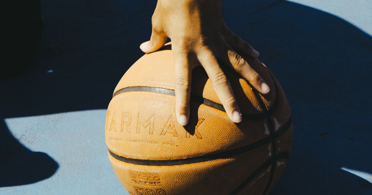 A hand resting on a basketball outdoors in bright sunlight